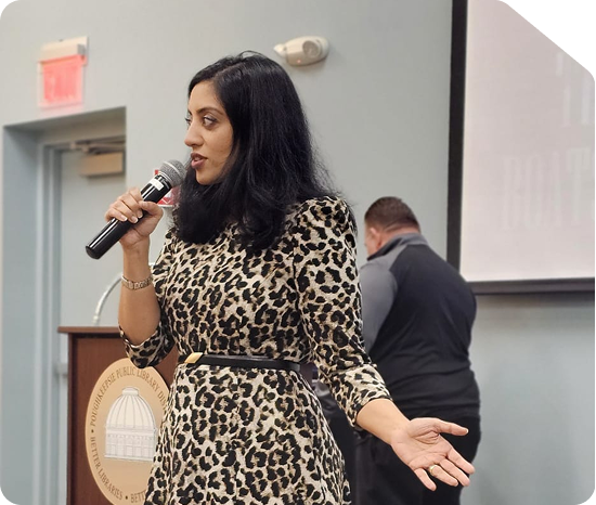 Angel Mary speaking into a microphone at a keynote event wearing a leopard print dress
